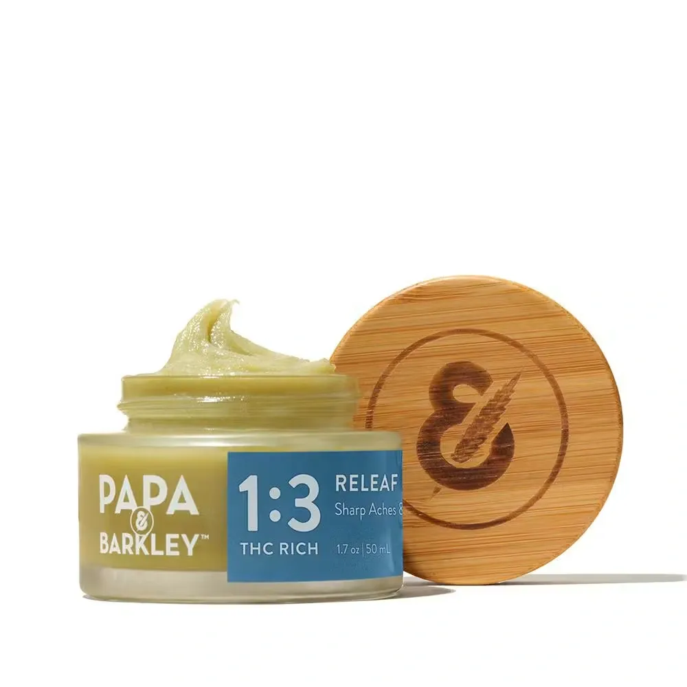 Open jar of Papa & Barkley 1:3 THC Rich Releaf Balm next to a wooden cap, available at Yerba Buena.